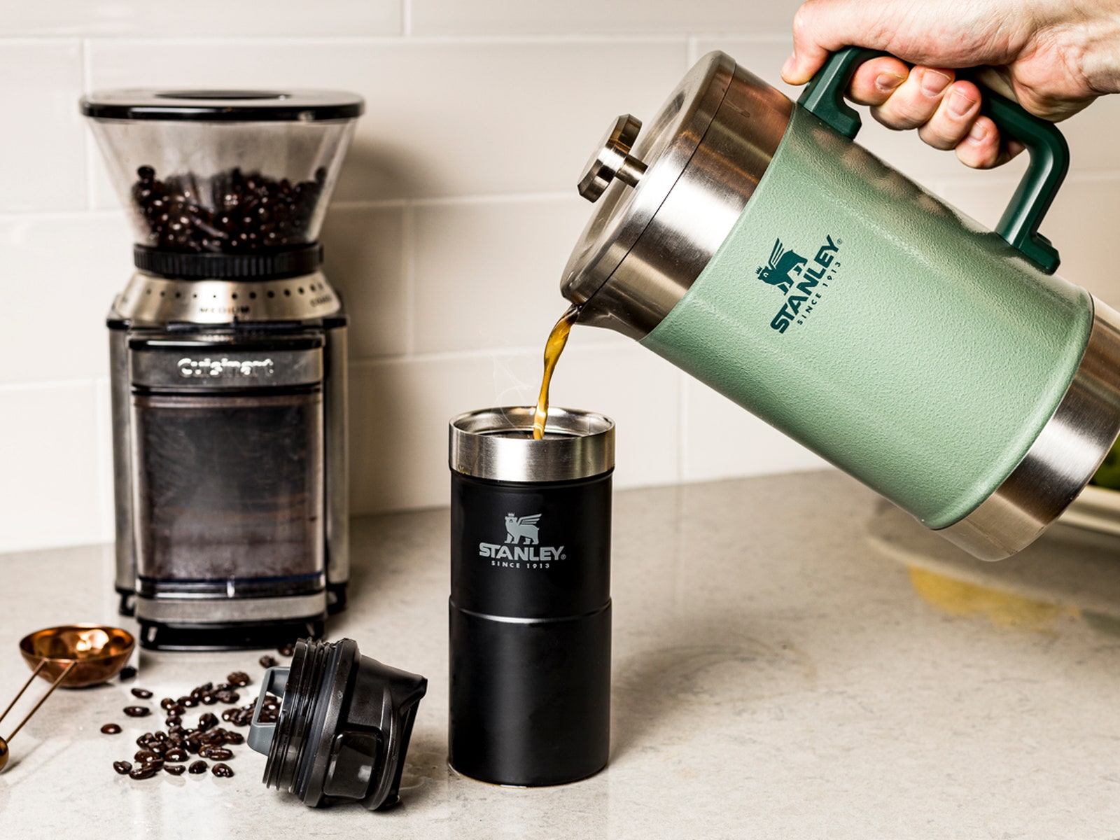Coffee from a french press being poured into a mug coffee beans and grinder on a kitchen counter